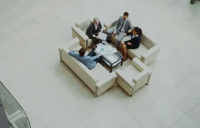 Group of professionals meeting on sofas in a bright atrium, discussing projects and listings for local businesses
